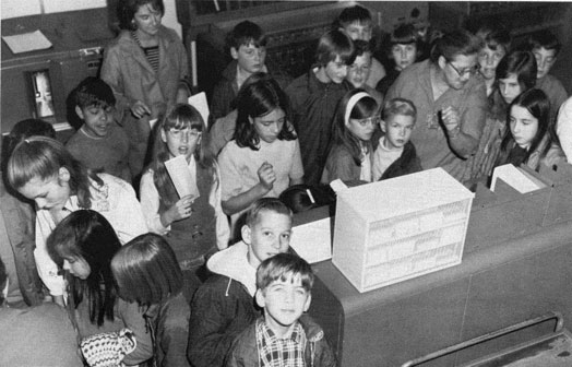 Children gathered around 'modern' punch card systems.